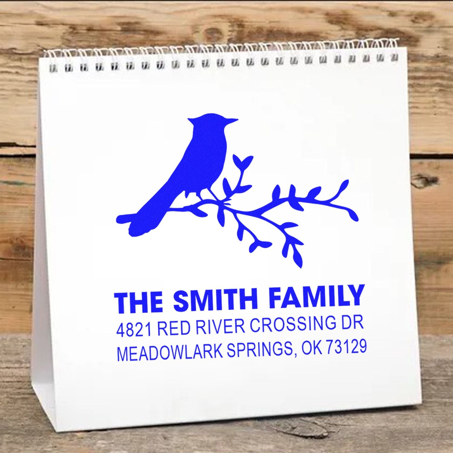Custom rubber stamp design with blue bird on branch and personalized family name, address, and city for return address or gift packaging.