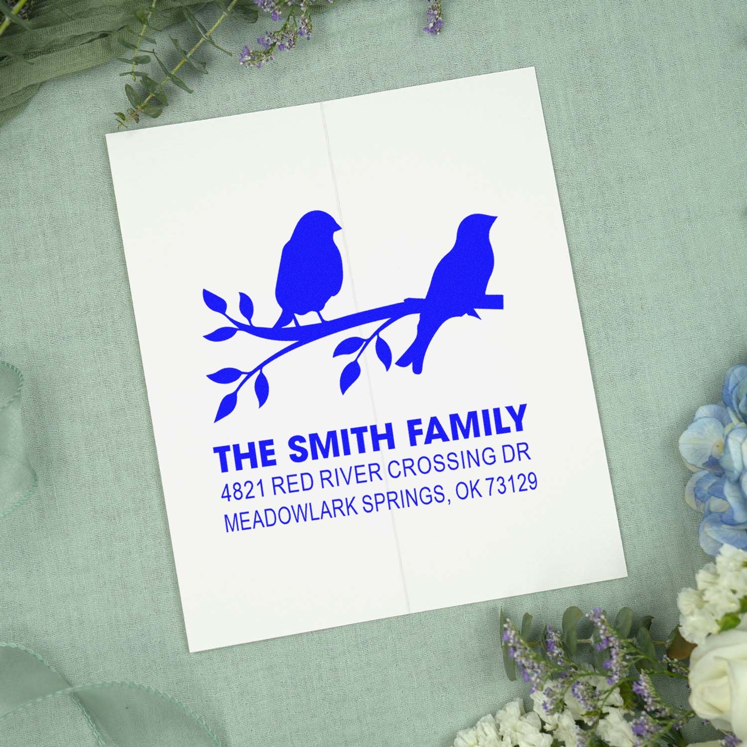 Custom self-inking return address stamp with two birds on a branch, personalized family name and address in bold blue for wedding or home mail.