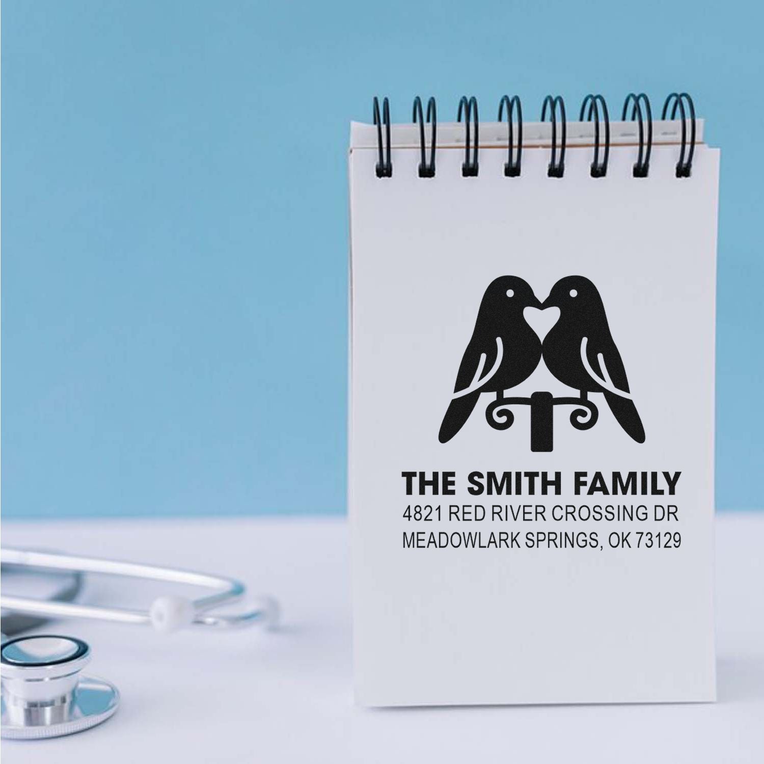 Personalized address rubber stamp with lovebirds design for The Smith Family, featuring custom name and return address on a desk notepad.