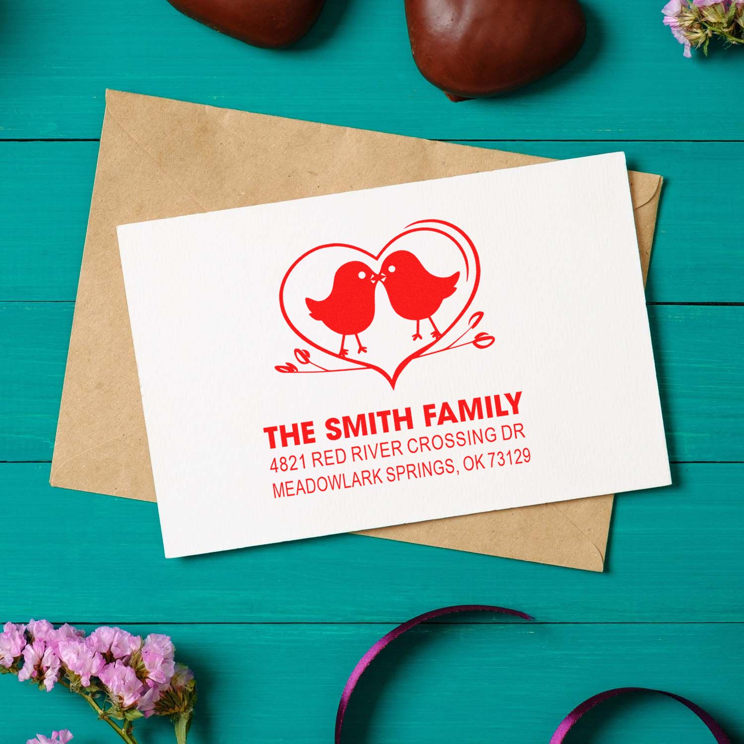 Custom return address rubber stamp with two birds in a heart design, featuring family name and address on white stationery envelope.