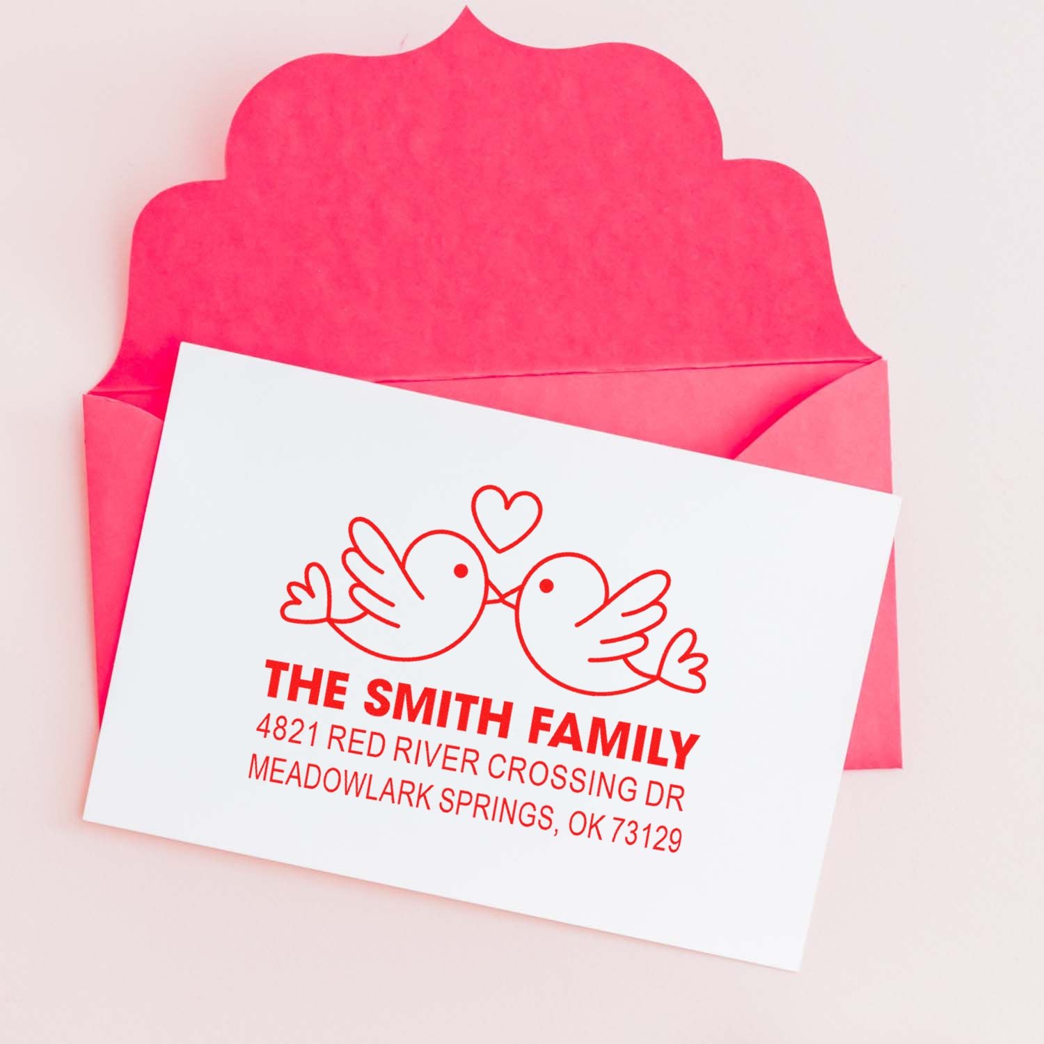 Custom return address rubber stamp with lovebird design on white card, shown with pink envelope, personalized family name and mailing address in red ink