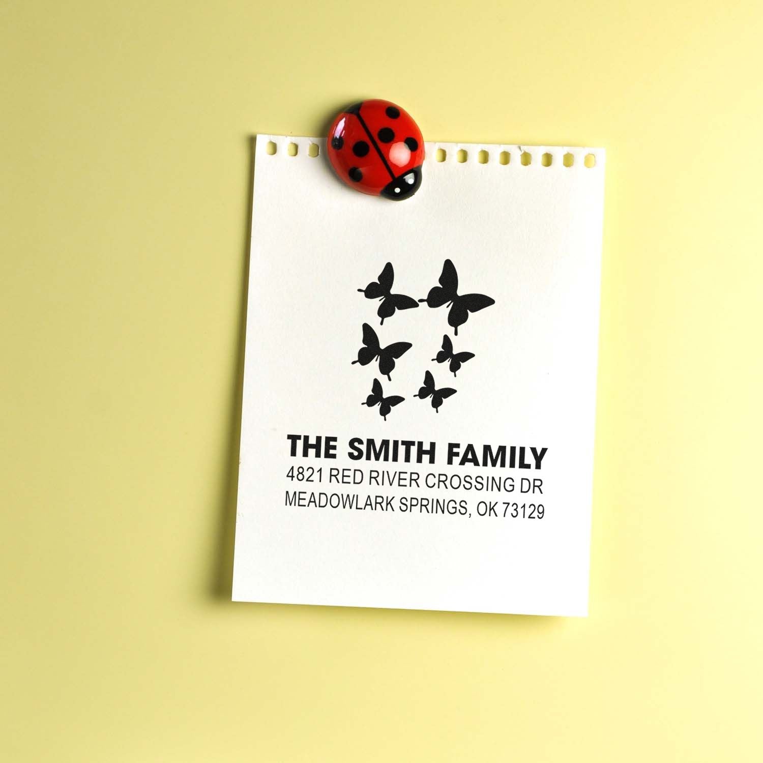 Custom address rubber stamp with butterfly design, The Smith Family name and address, shown on white paper with a red ladybug clip accent.