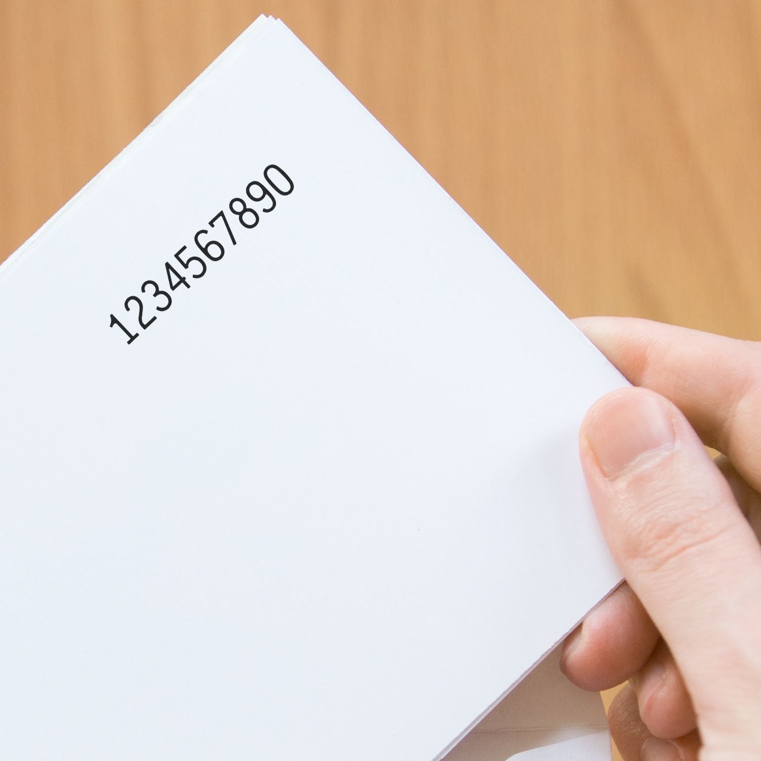 Hand holding a white card with printed numbers 1234567890 on a wooden background.