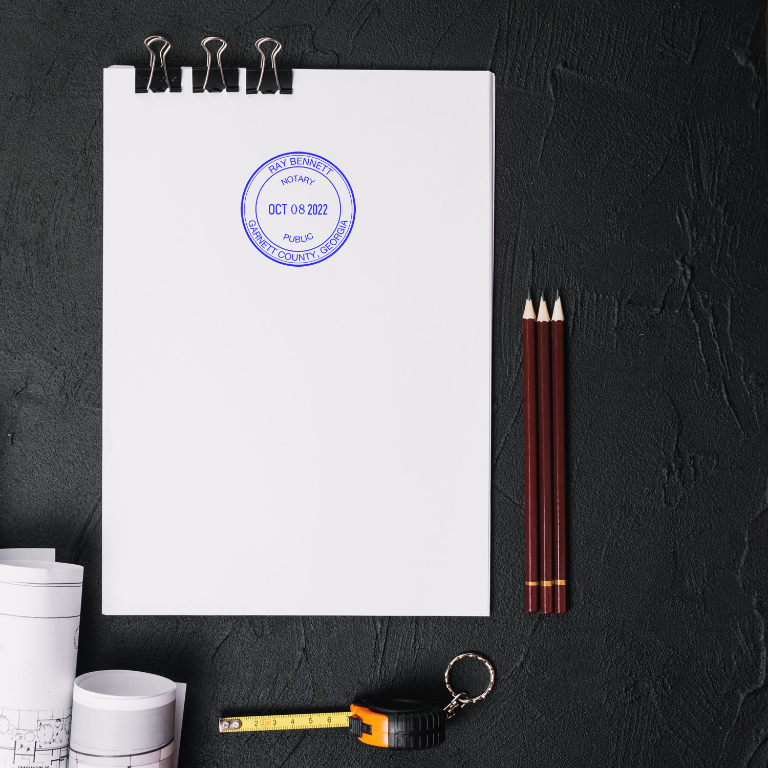 Notarized blank document on clipboard with pencils, tape measure, and rolled blueprints on black desk, legal office stationery and real estate planning concept