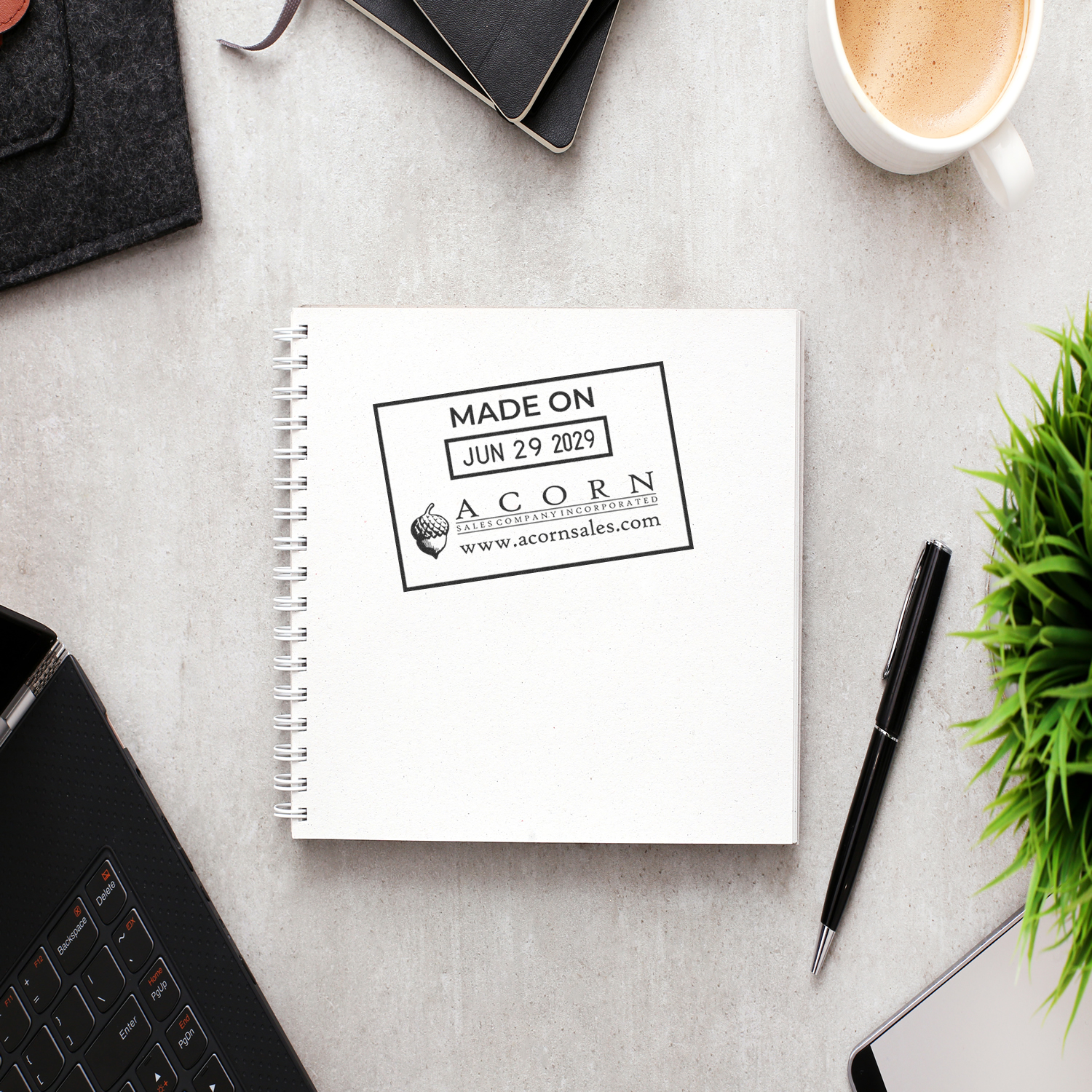 Minimal office desk flat lay with blank spiral notebook, coffee cup, laptop, pen, and green plant on a light stone background.