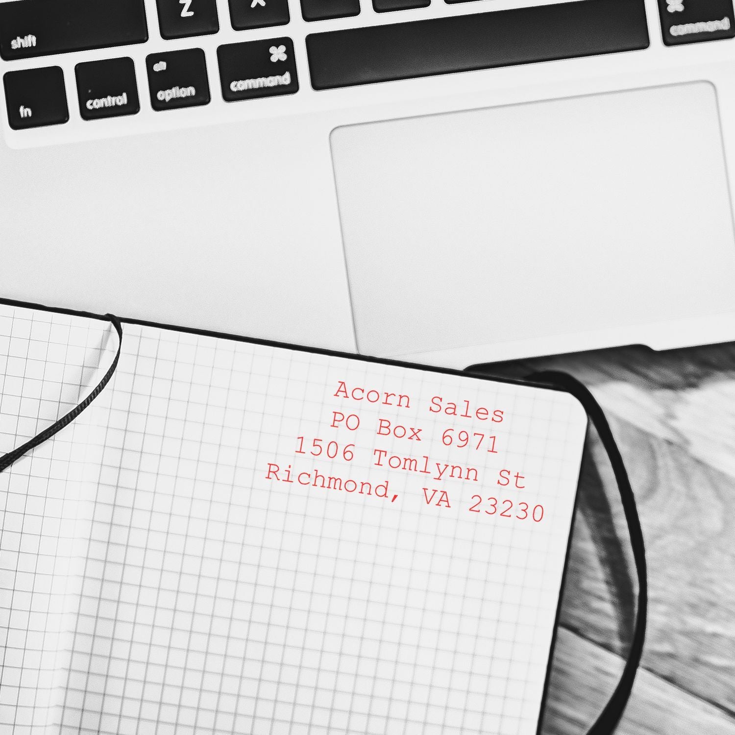 Close-up of a MacBook keyboard, notebook, and addressed envelope with red mailing stamp on a desk.