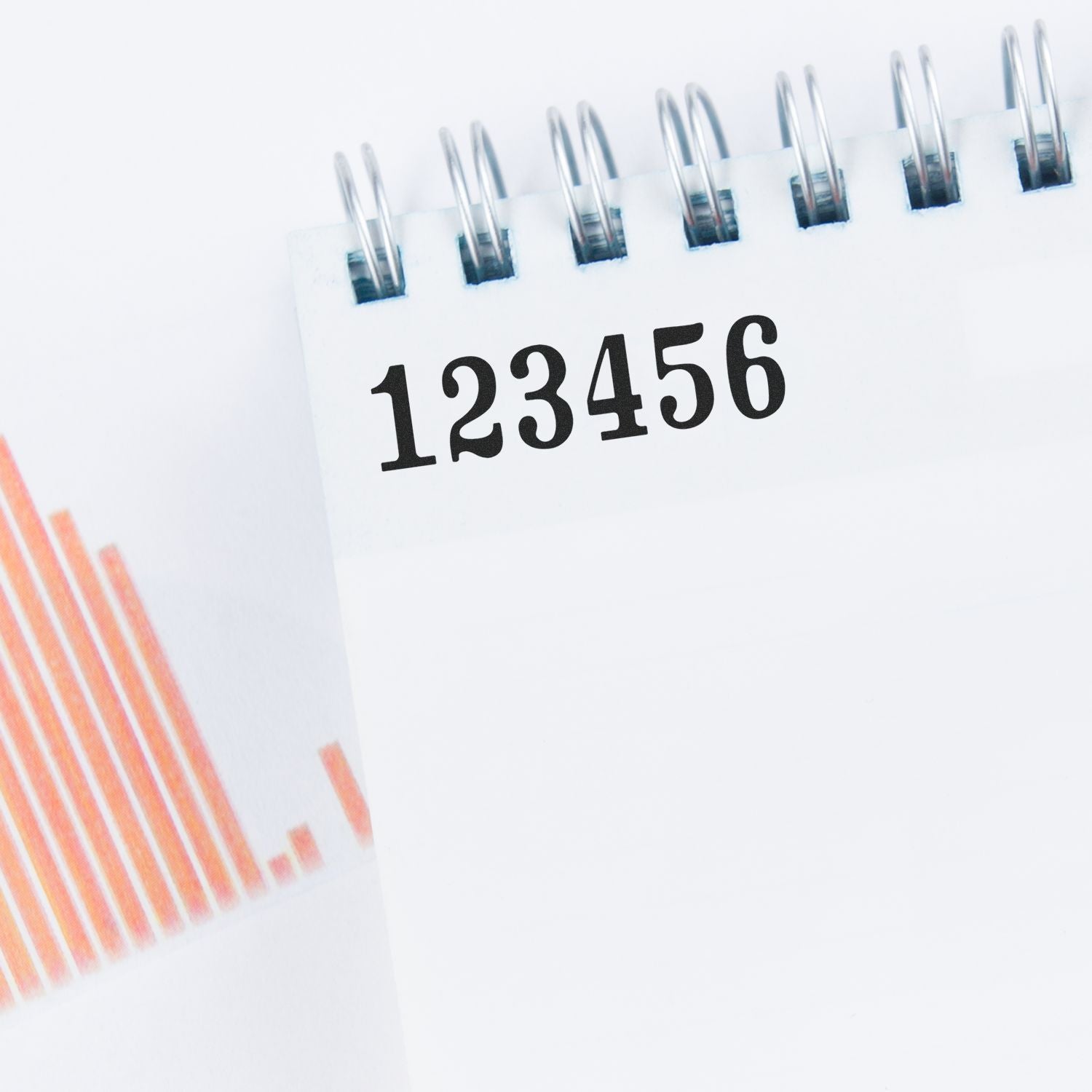 Close-up of spiral notebook with 123456 on a page beside orange financial chart bars, business data concept.