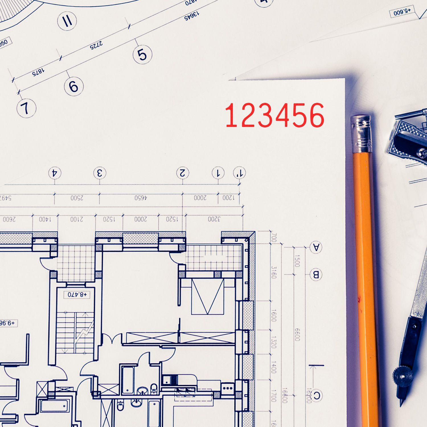 Architectural floor plan blueprint with pencil and drafting tools on a white desk.