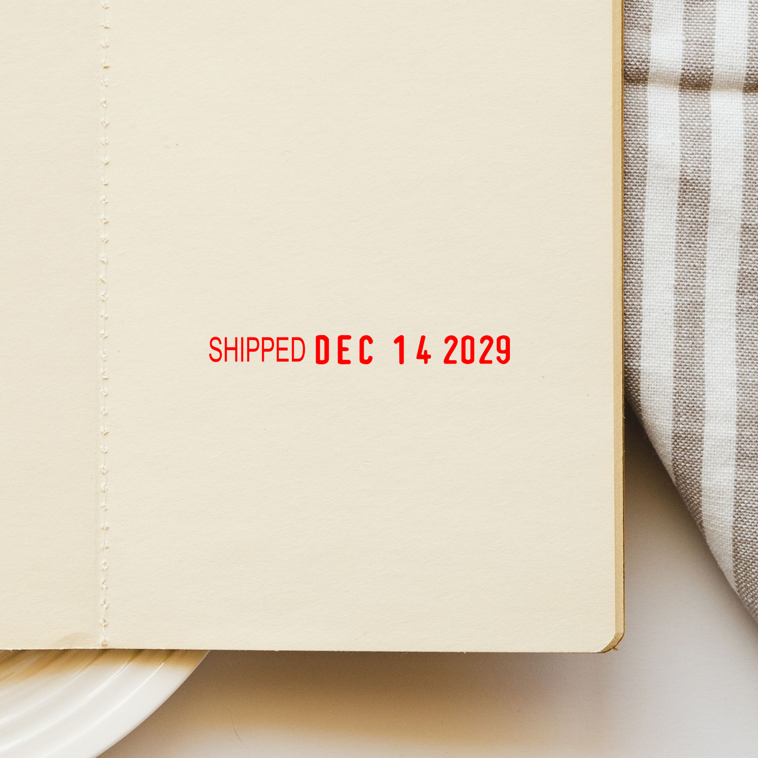 Minimal notebook page with red Shipped Dec 14 2029 text, flat lay stationery background with fabric and plate.