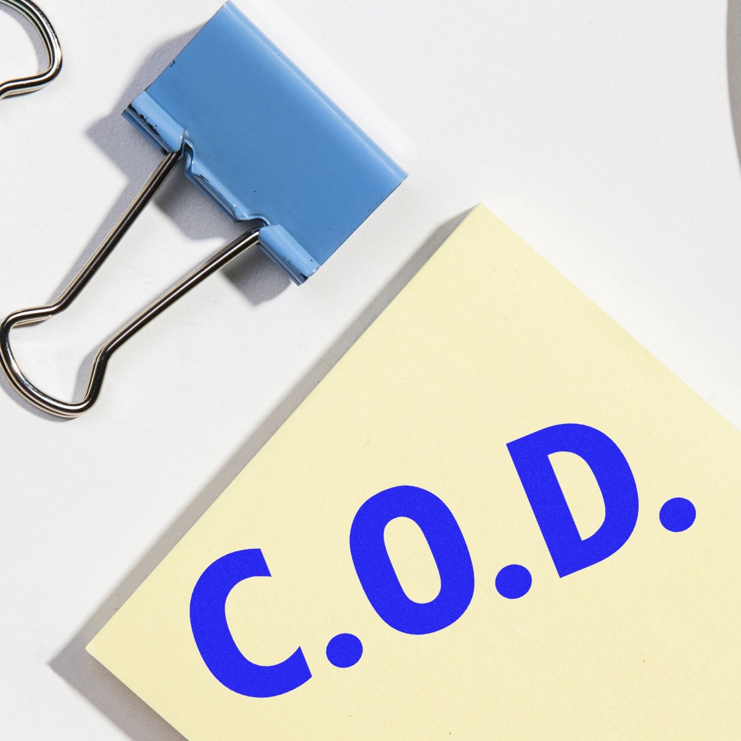 Binder clips hold a yellow paper card showing a large blue 0. symbol and dot, representing product pricing or numeric value info