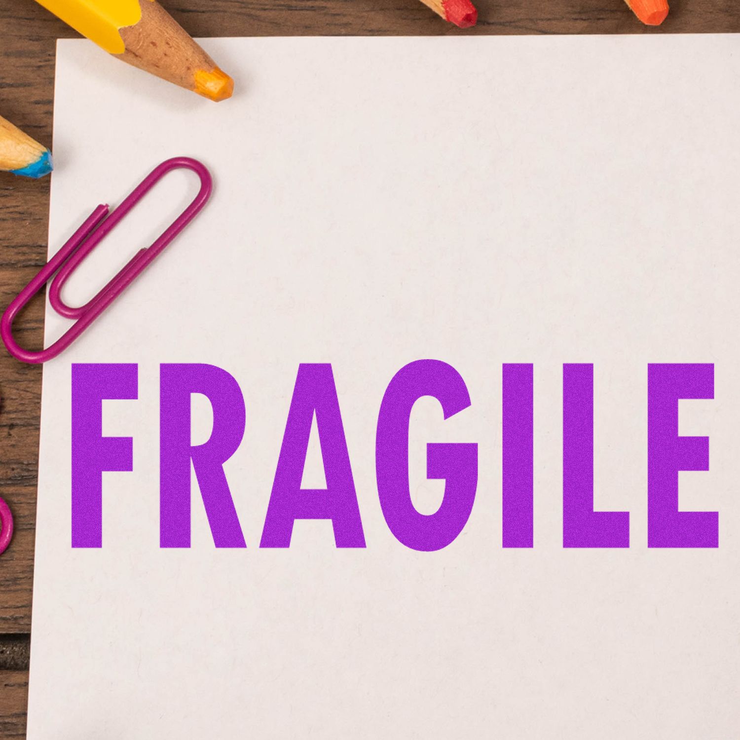 FRAGILE label on white shipping paper with bold purple lettering and stationery on a wooden desk, indicating safe package handling.