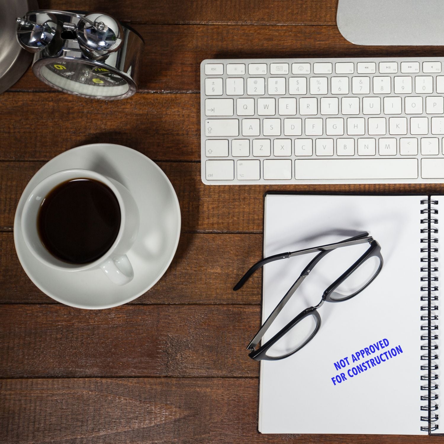 Top view of laptop keyboard, coffee, magnifying glass, and notebook with Not approved for constructionplanning and review desk