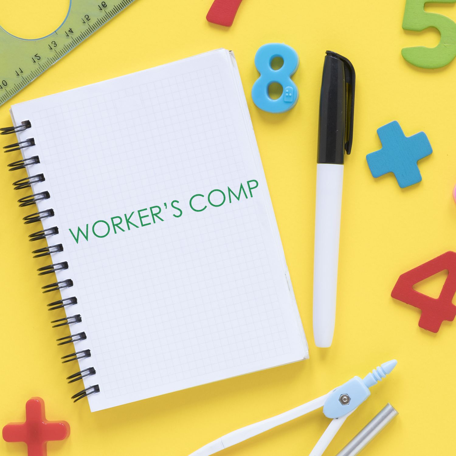 Notebook labeled WORKER'S COMP with pen, marker, ruler and blocks on yellow backgroundworkers compensation insurance awareness.