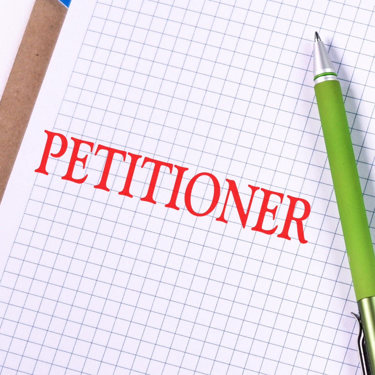 Close-up of PETITIONER text on grid notebook paper with a green pen, illustrating petition preparation for court filings and legal paperwork.