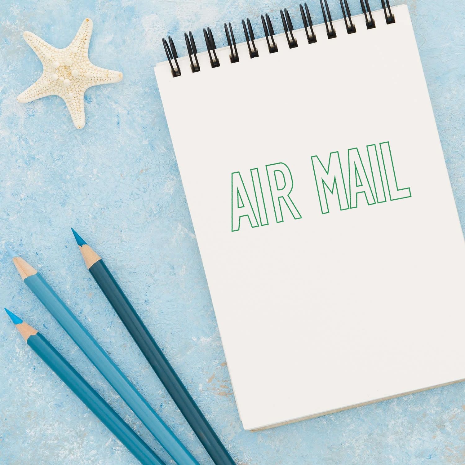 Air mail travel notebook with starfish and pencils on blue background, promoting coastal stationery and vacation planning ideas.