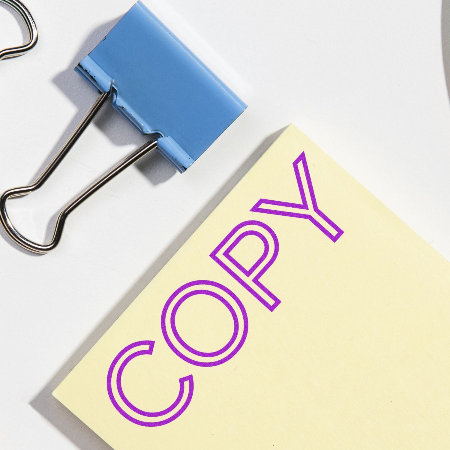Blue binder clip holds a yellow office stationery page with a purple graphic, illustrating document organization with clips.