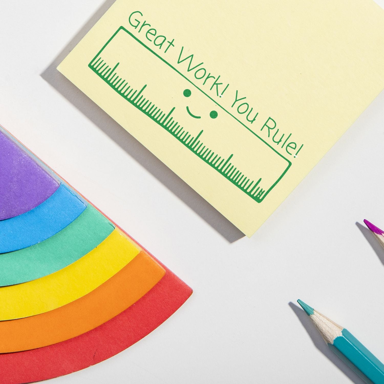 Close-up of a yellow note reading Great Work! with green ruler design, surrounded by colorful crayons for classroom motivation.