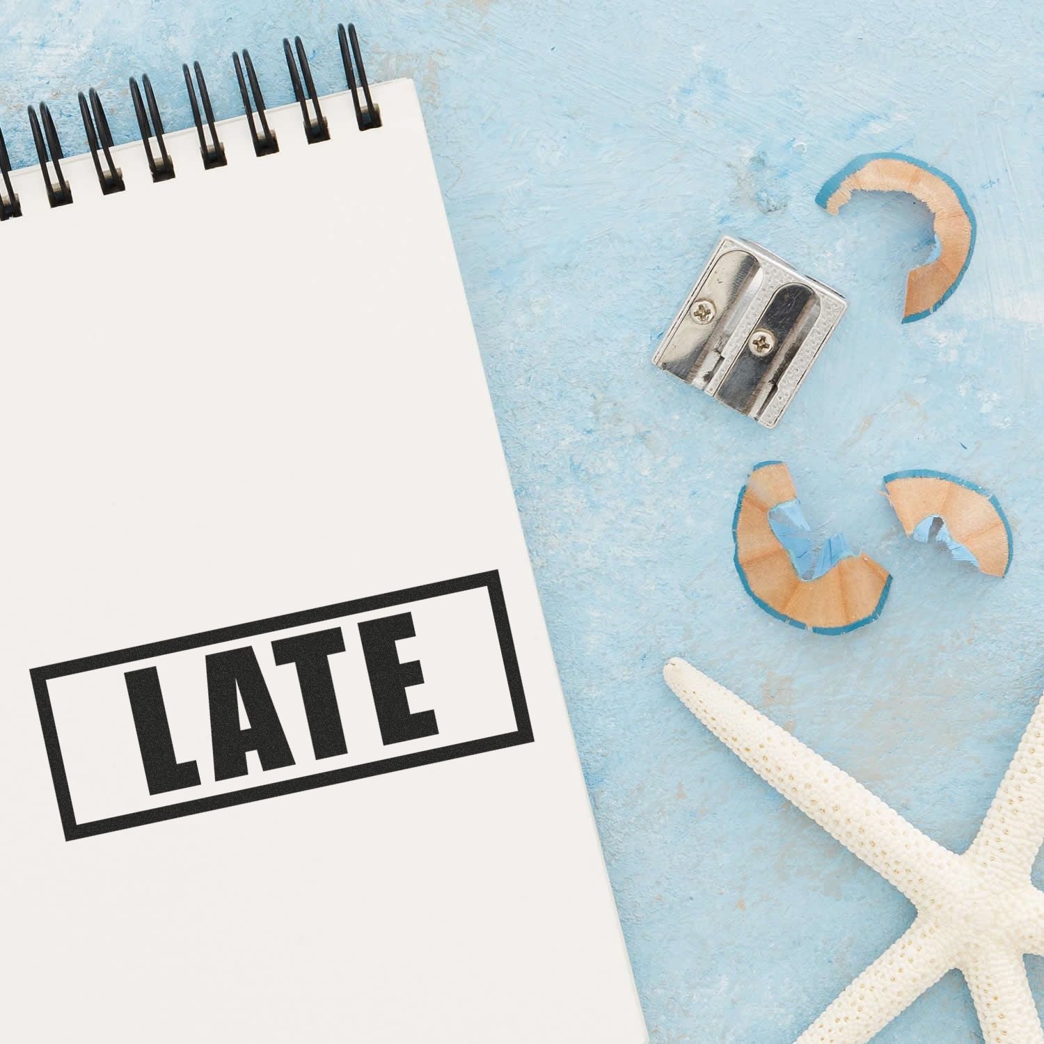 Beach-themed stationery flat lay with pencil sharpener, starfish, and notebook showing LATE message.