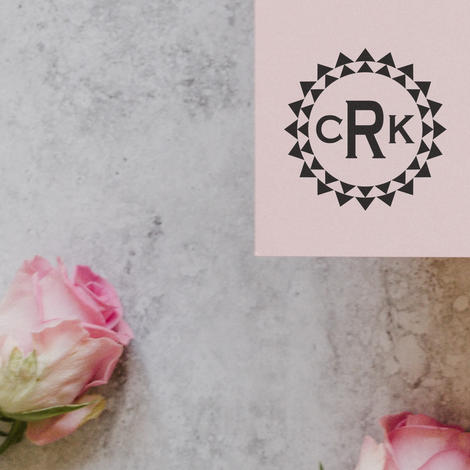 Personalized monogram rubber stamp with geometric circle logo on pink card, styled with roses on a marble background.