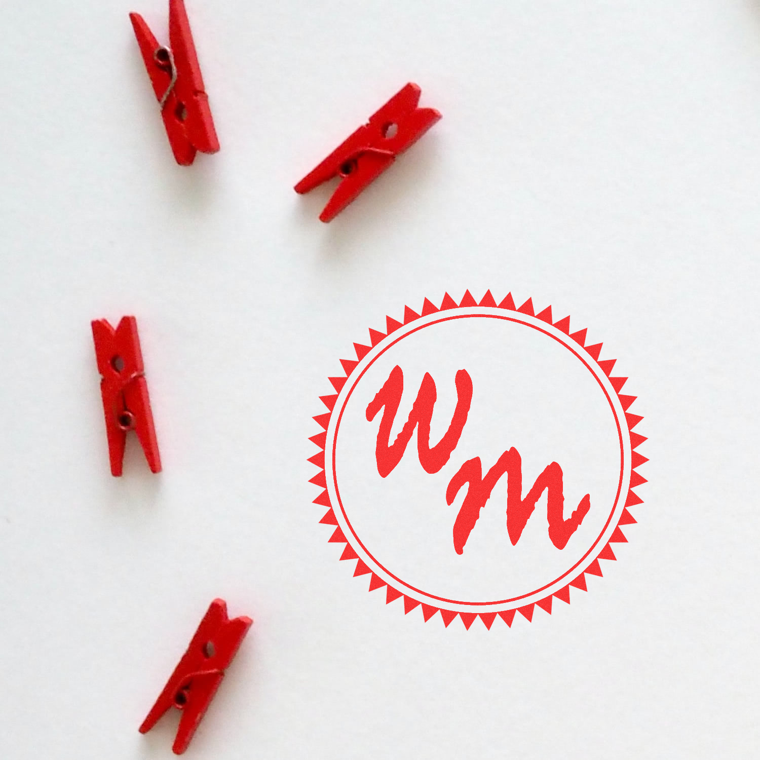 Custom red rubber stamp design with WM monogram and decorative clip accents on a white background.