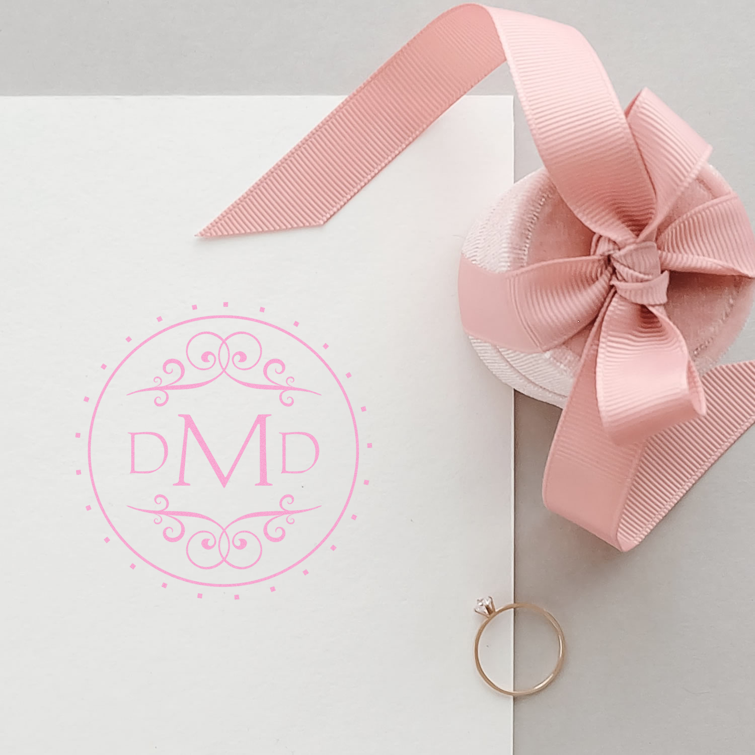Custom pink monogram rubber stamp on a wedding invitation, with ribbon bow, for personalized stationery and branding.