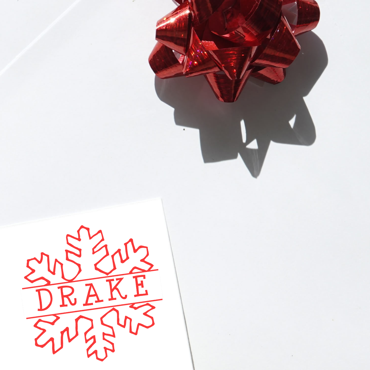 Custom rubber stamp impression with DRAKE and maple leaf design on white paper, shown beside a red gift bow.