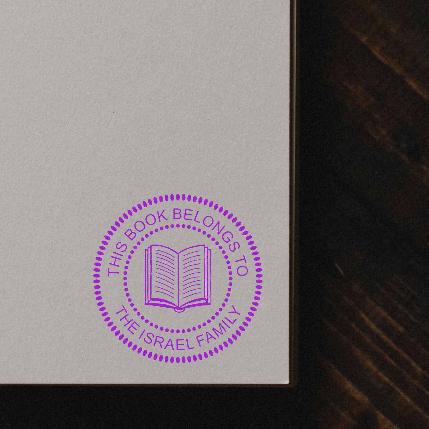 Custom rubber book stamp with open book icon and text, This book belongs to the Israel Family in purple.