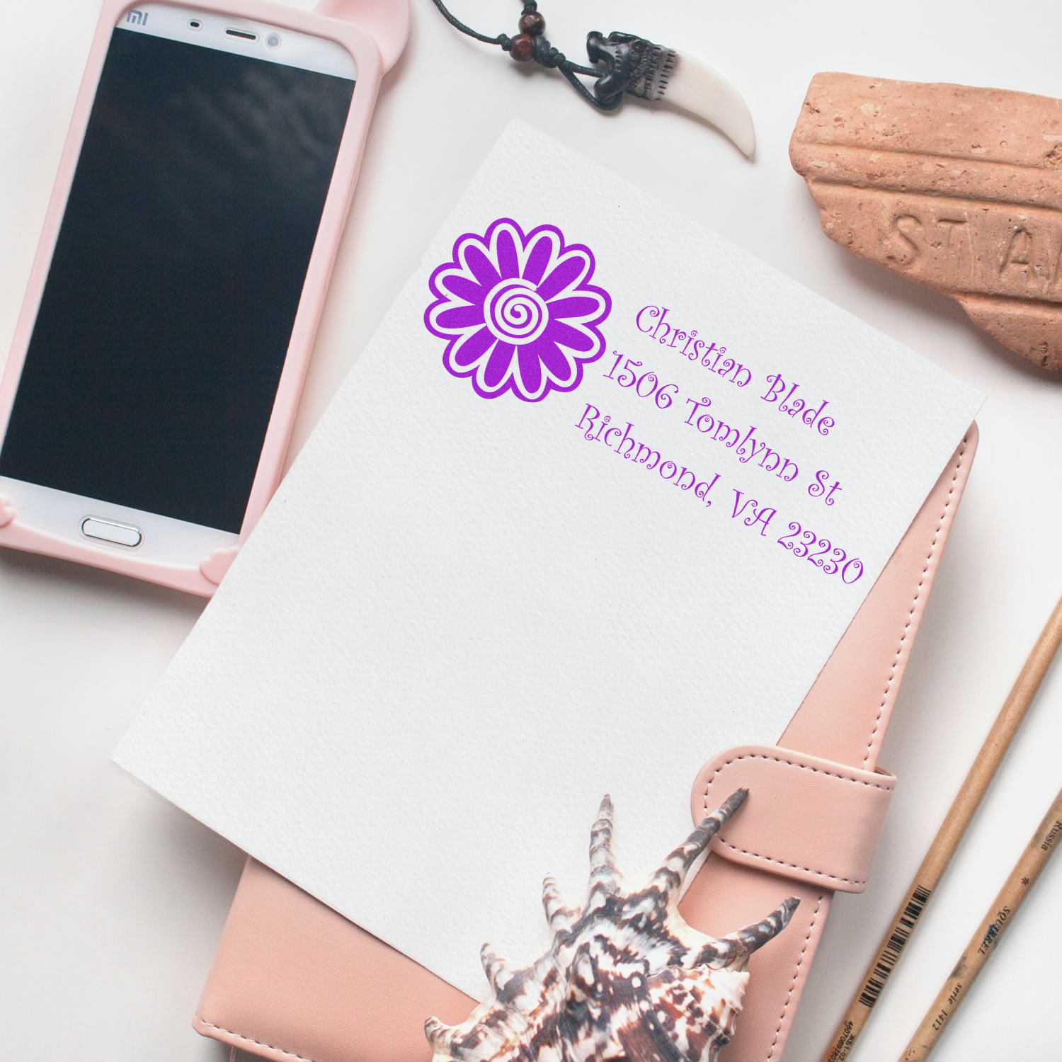 Custom floral address rubber stamp on notebook, showing a purple monogram name and return address design.