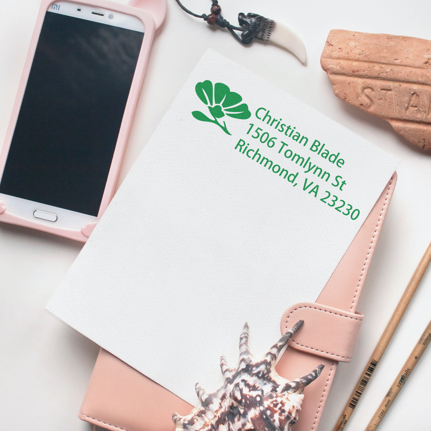 Custom rubber return address stamp with green floral logo and Christian Blade address on a notebook.