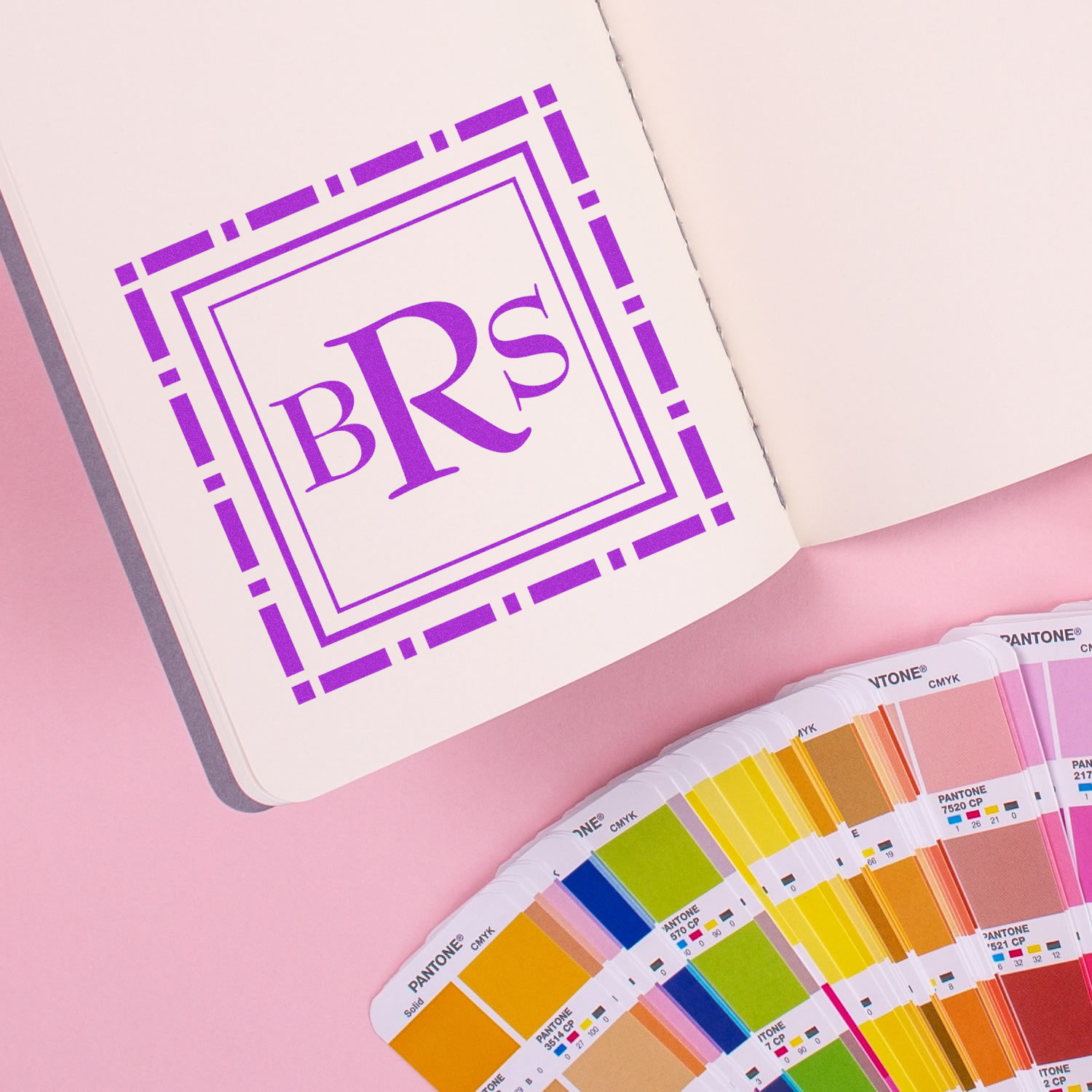 Custom purple BRs rubber stamp logo on notebook with Pantone color swatches, showcasing branded stationery design.