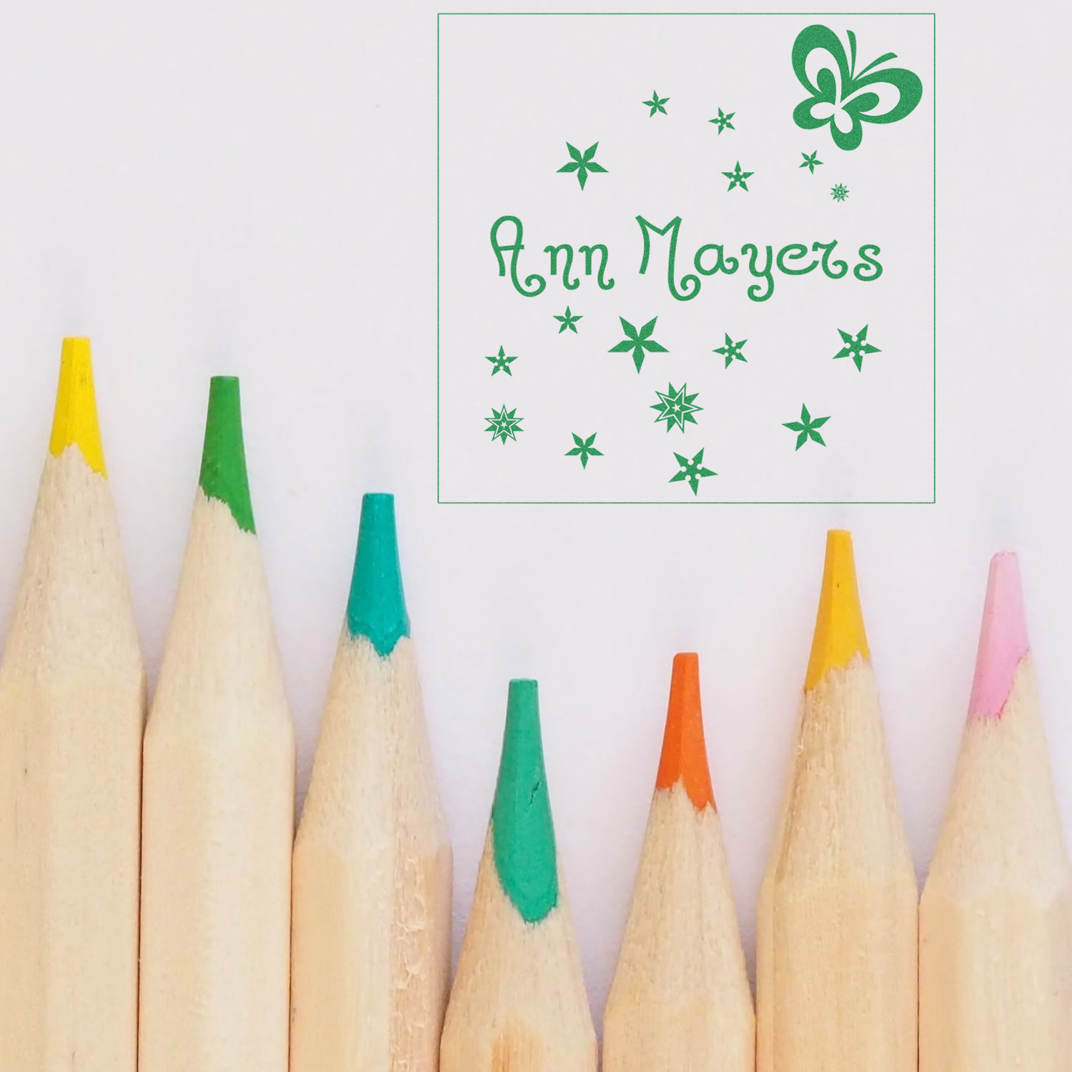 Custom rubber stamp design reading Ann Moyers with stars and butterfly, shown above colored pencil tips.