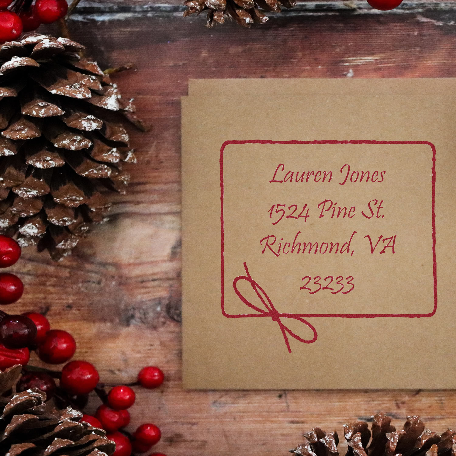 Custom return address rubber stamp on kraft envelope with festive pinecones and berries.