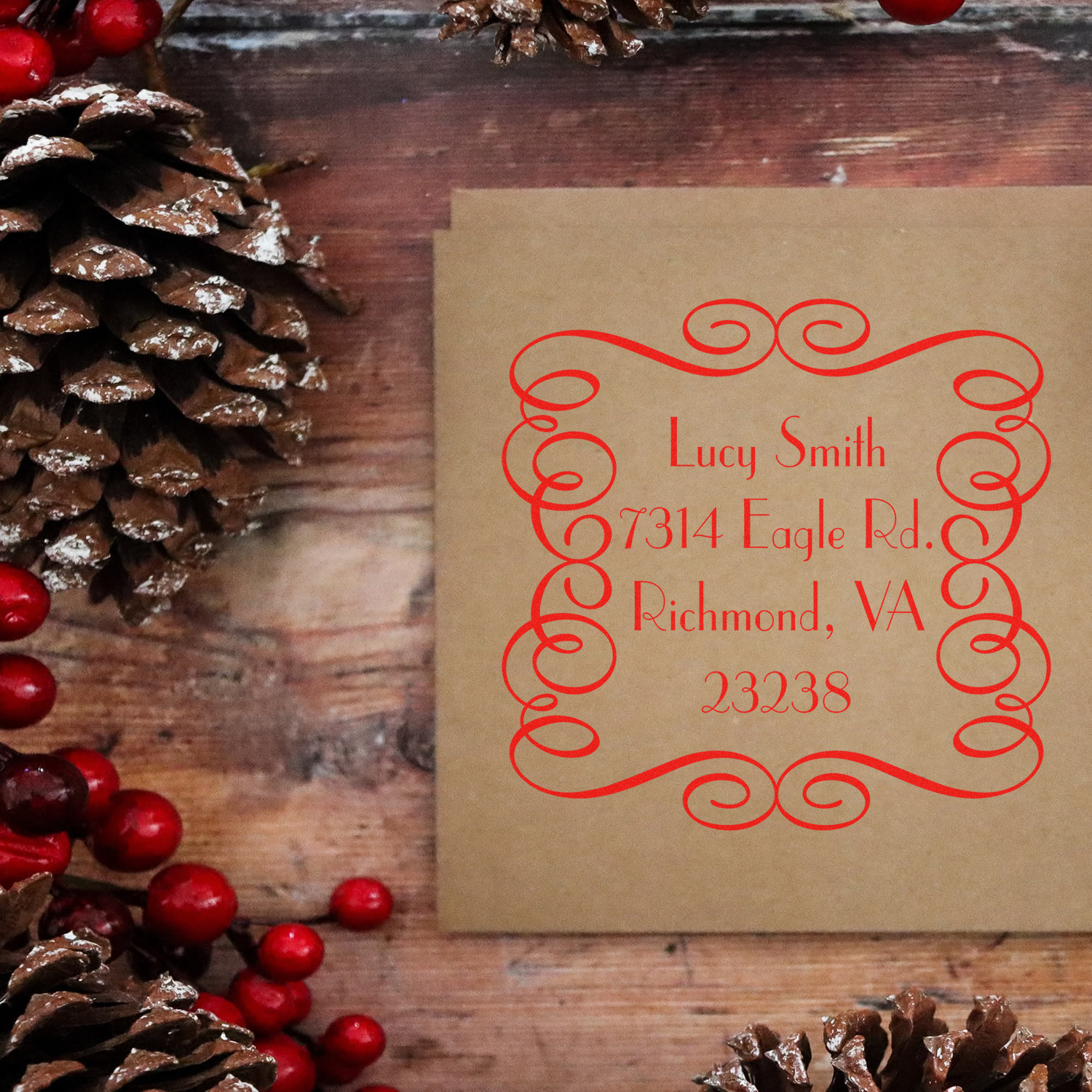Personalized return address rubber stamp on kraft envelope with ornate red address design and holiday pinecone decor.