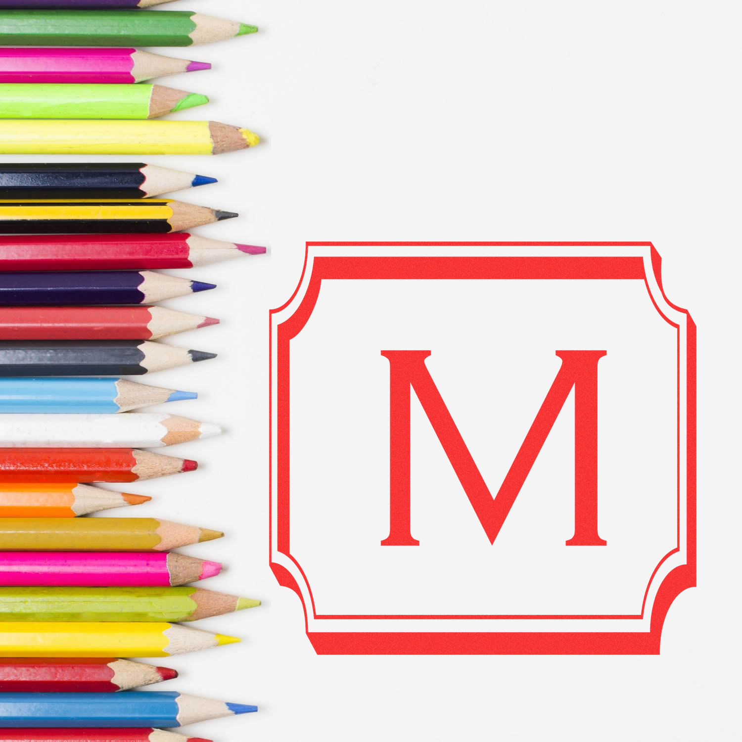 Custom rubber stamp monogram M design beside colorful pencils on a white background