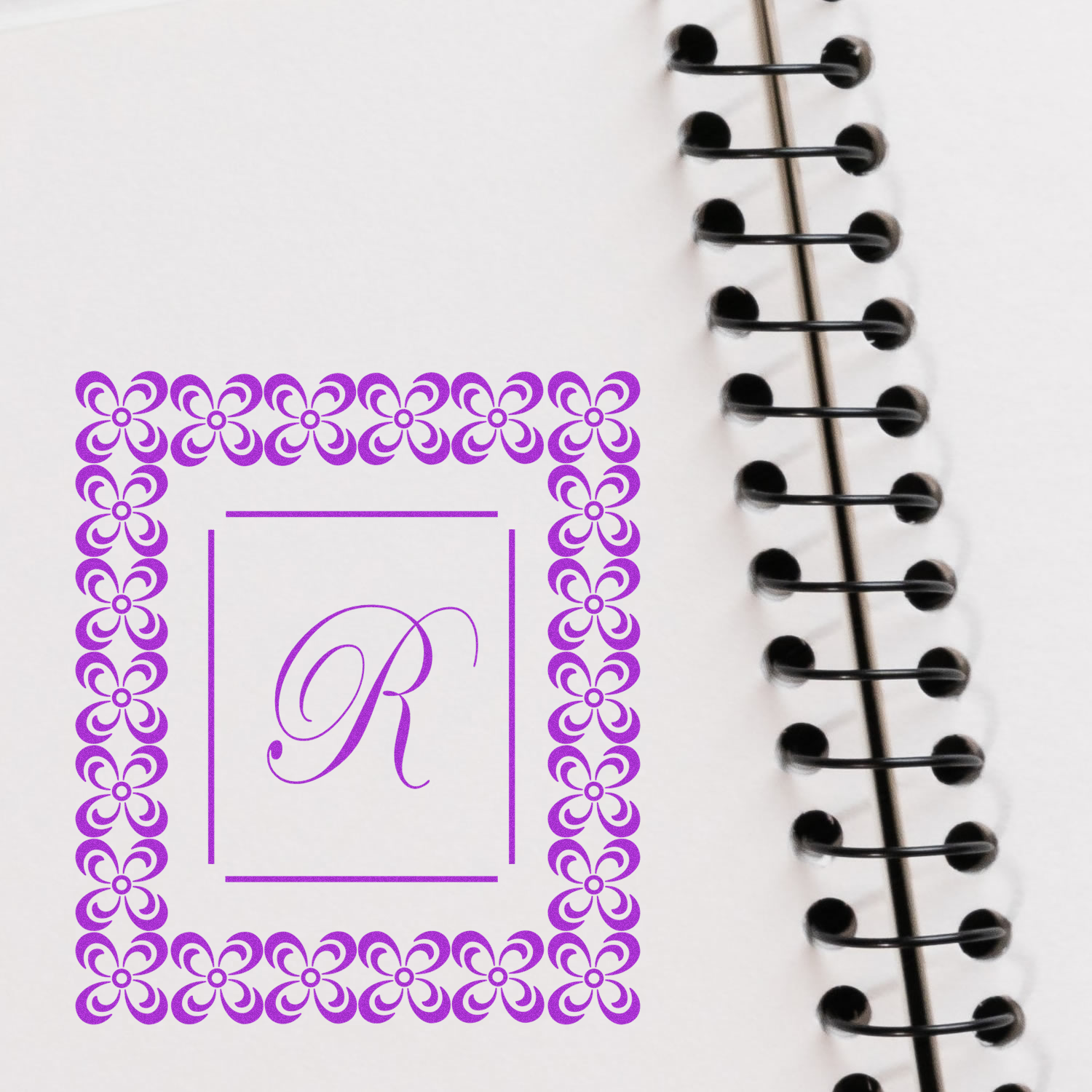 Custom floral monogram R rubber stamp design printed on notebook paper beside spiral binding.