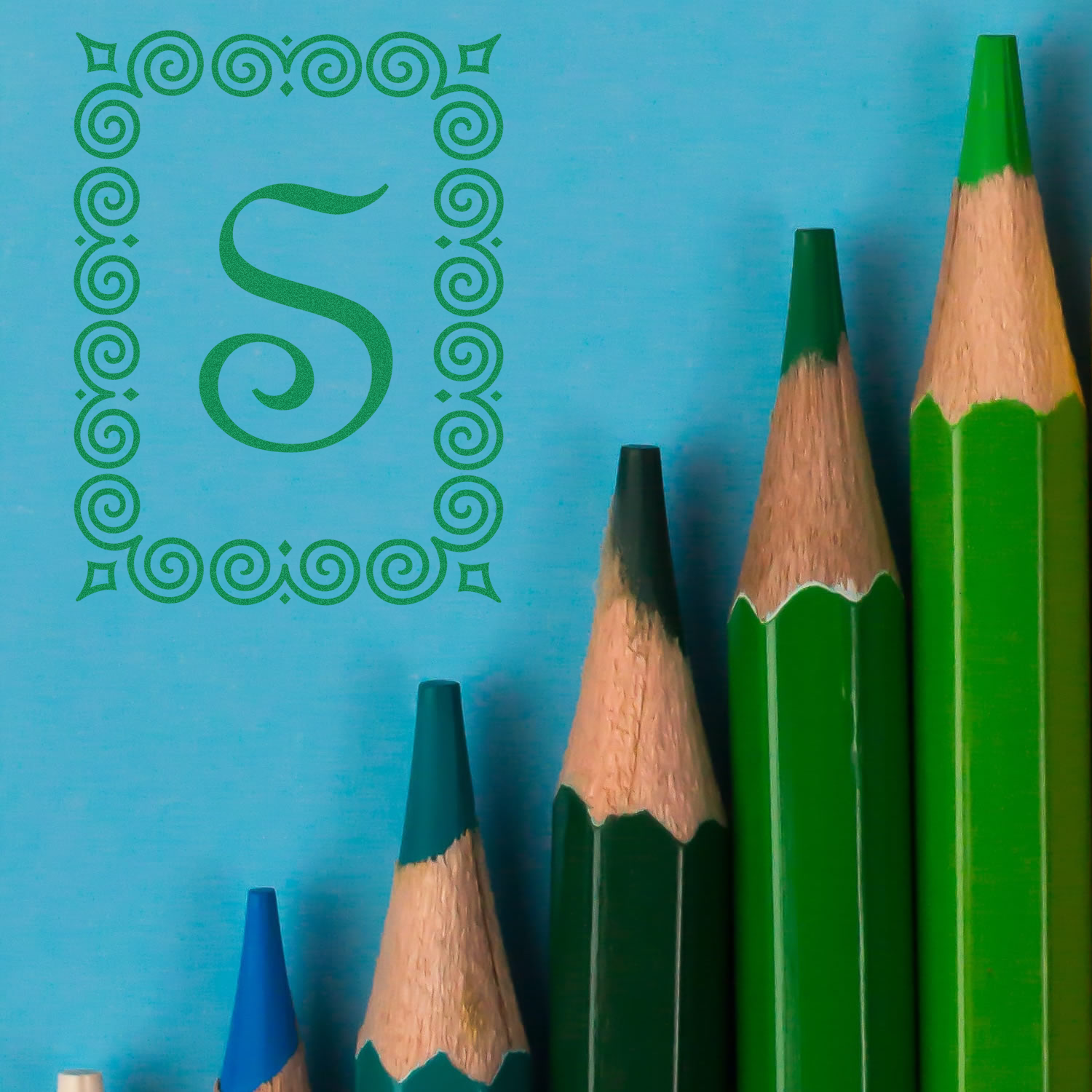 Illustrated letter S made with green pencil spirals on blue background, with colored drawing pencils for stationery branding