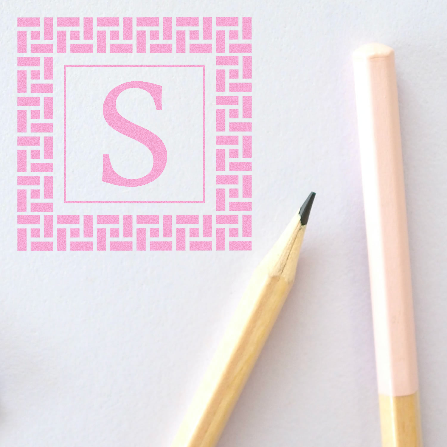 Pink S monogram rubber stamp design with decorative border, shown on paper with pencil for custom stationery branding