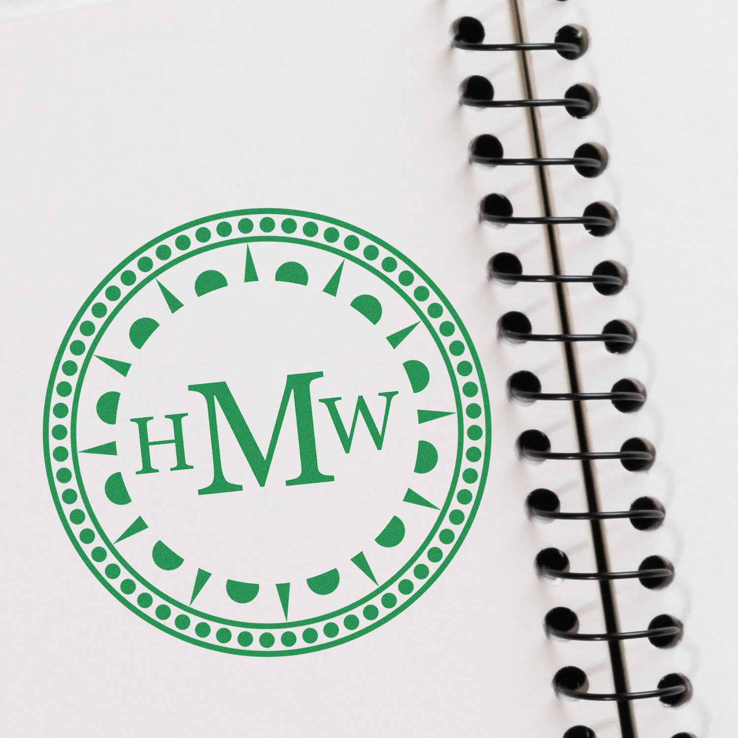 Green HIW circular stamp on a white notebook with spiral binding, used for stationery branding and study planning with a custom logo.