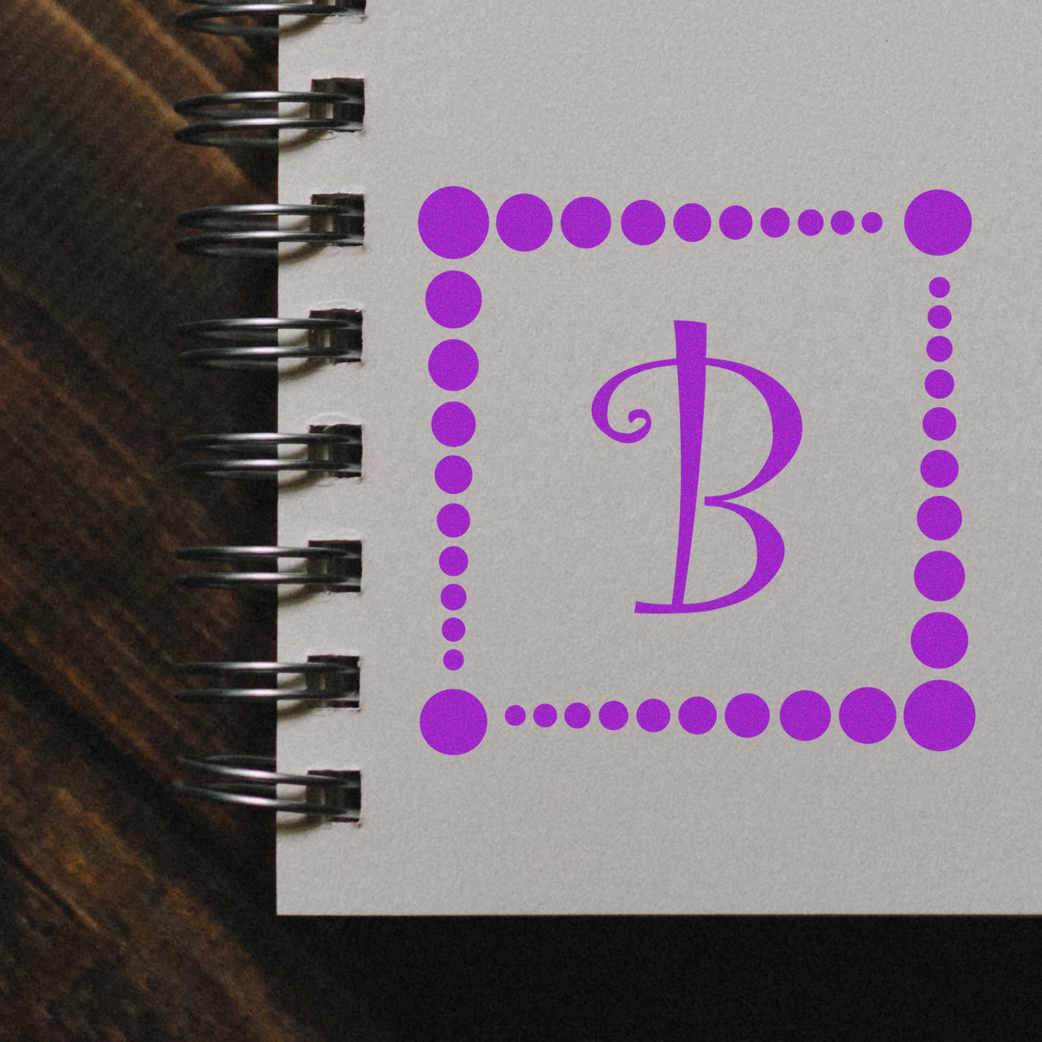Custom monogram B rubber stamp design with dotted border on notebook page for stationery branding.