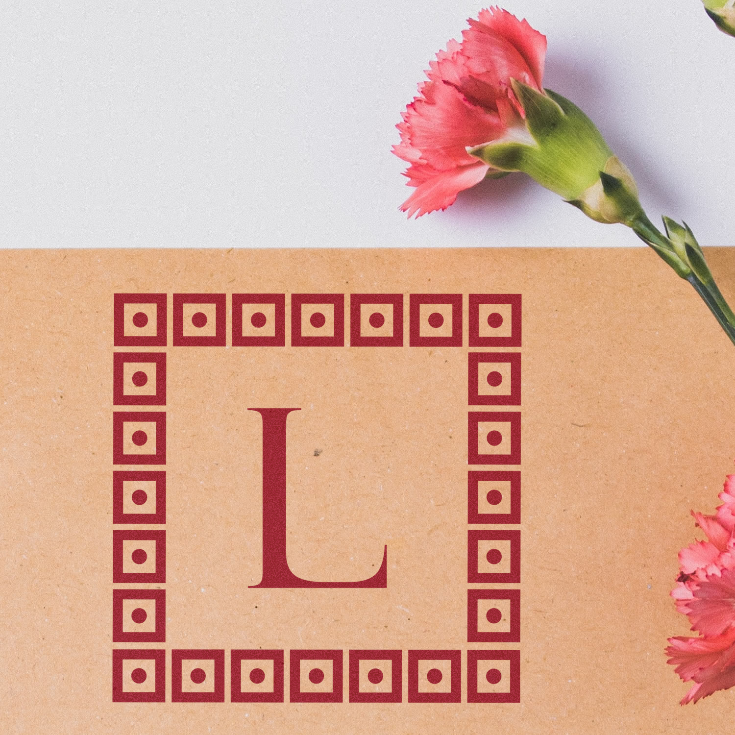 Custom L initial rubber stamp design with geometric border, shown on kraft paper with pink carnations.