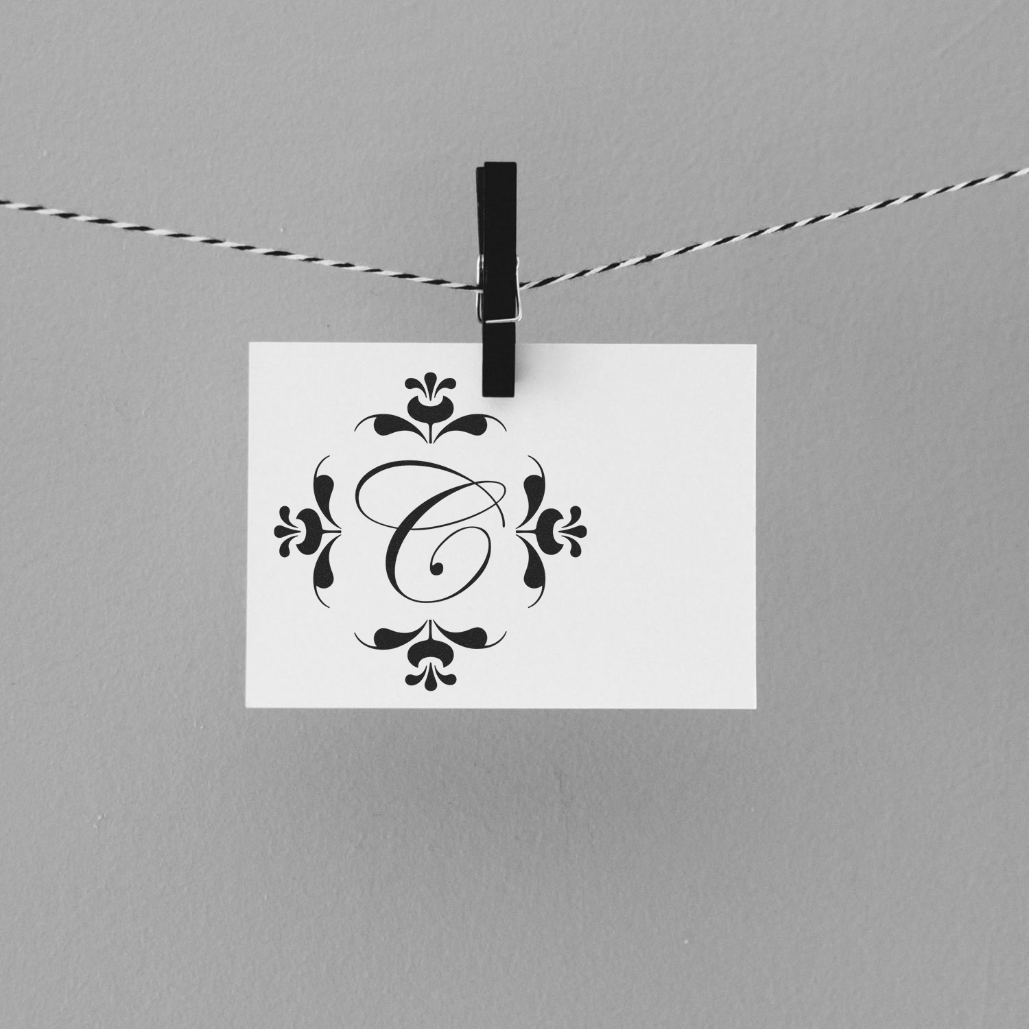Clothespin holds a decorative floral monogram card on a string, symbolizing handmade branding and creative design presentation.