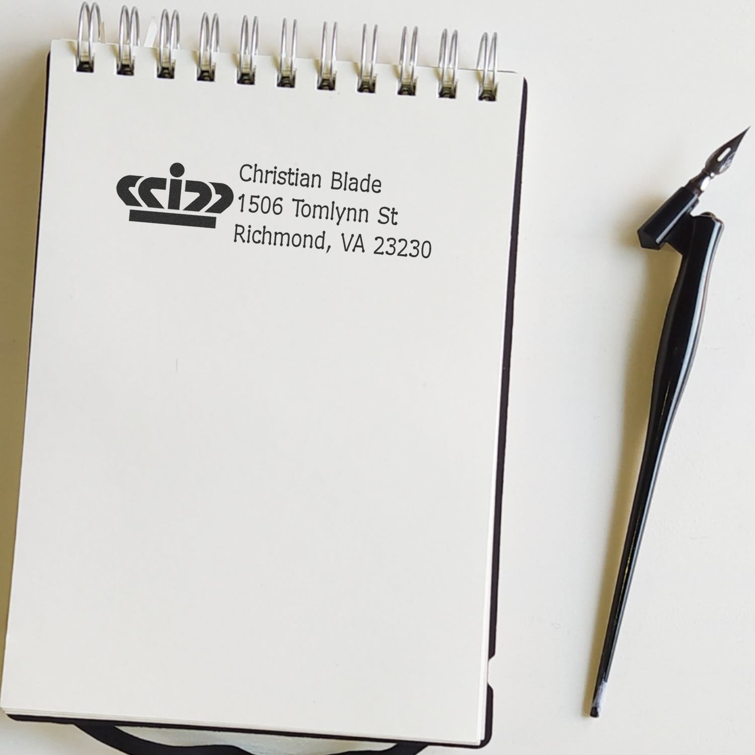 Custom logo address rubber stamp impression on notebook, beside fountain pen nib.
