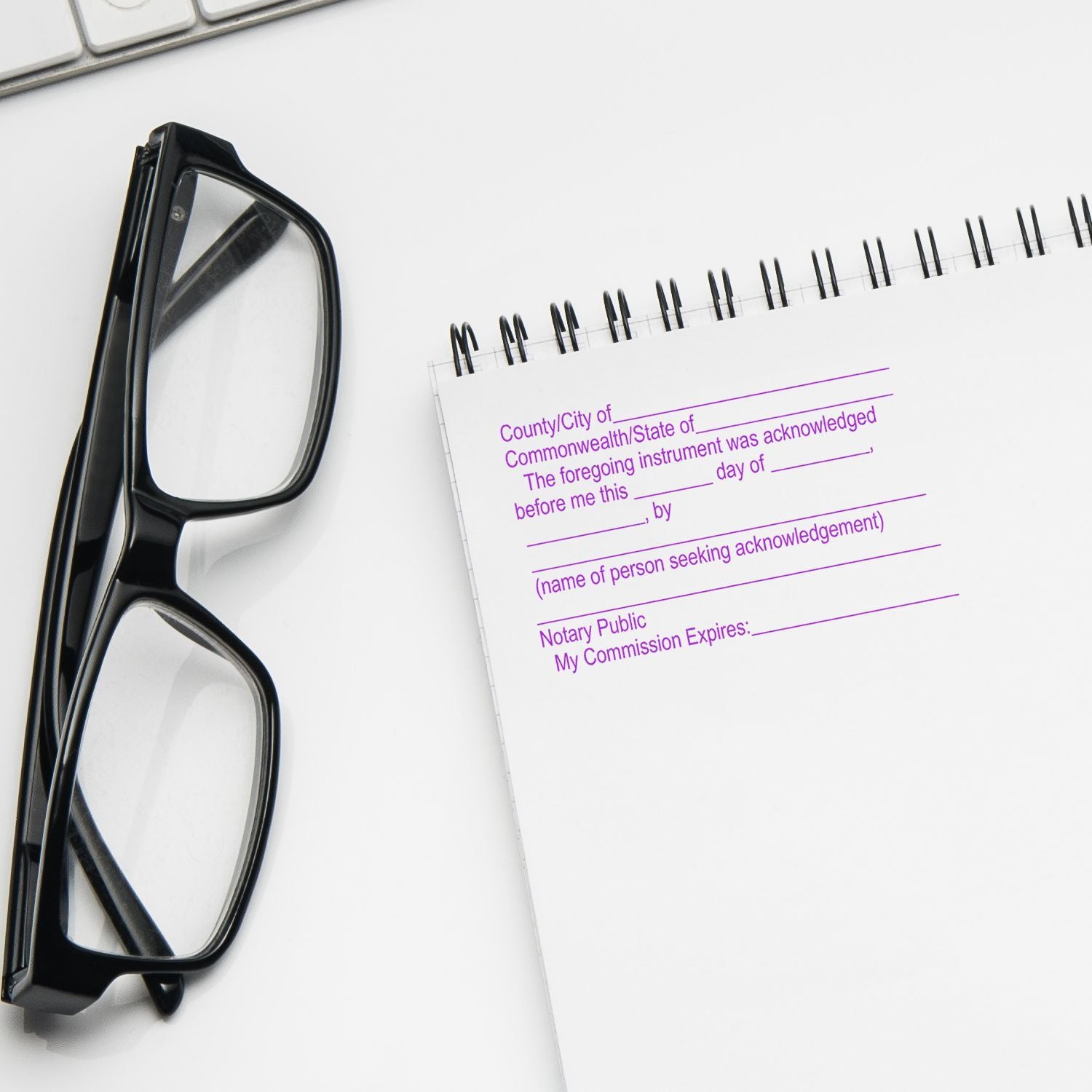 Black eyeglasses beside a notary public acknowledgment journal on a white desk.