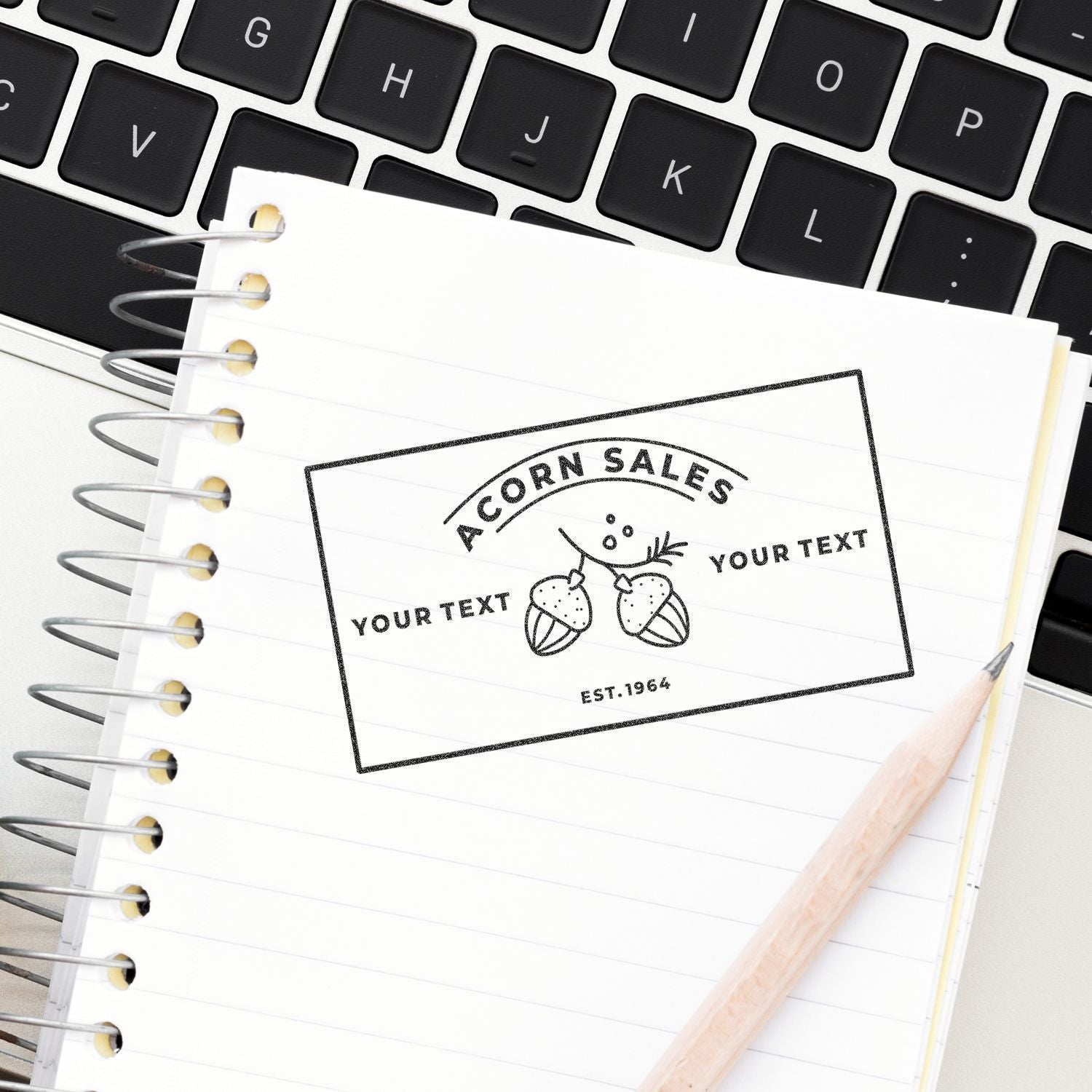 Spiral notebook with custom Acorn Sales logo mockup on laptop keyboard, with pencil and branding design concept.