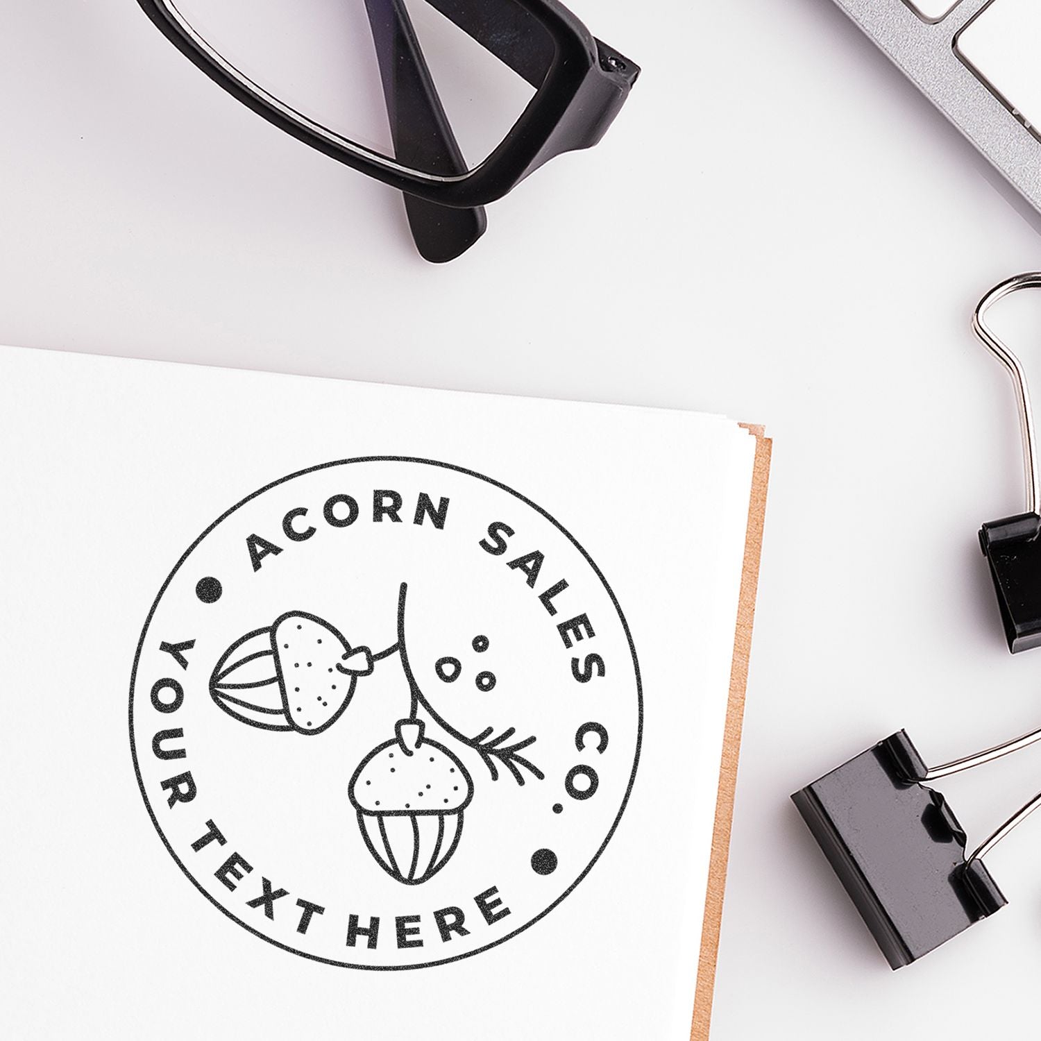 Acorn Sales branding logo stamp on paper with office stationerypencil, binder clips, and notebook for marketing business strategy.