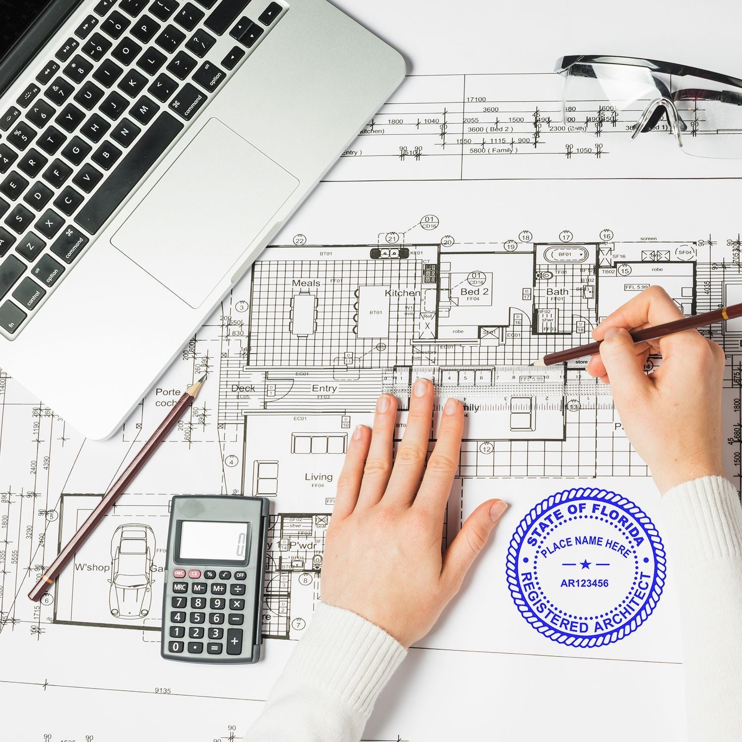Architect reviewing house floor plan blueprint with laptop, calculator, ruler, and drafting tools on desk.