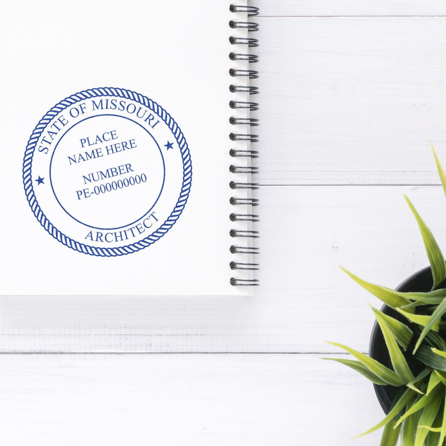 Missouri architect stamp on a white spiral notebook with a small green potted plant on a white wooden desk.