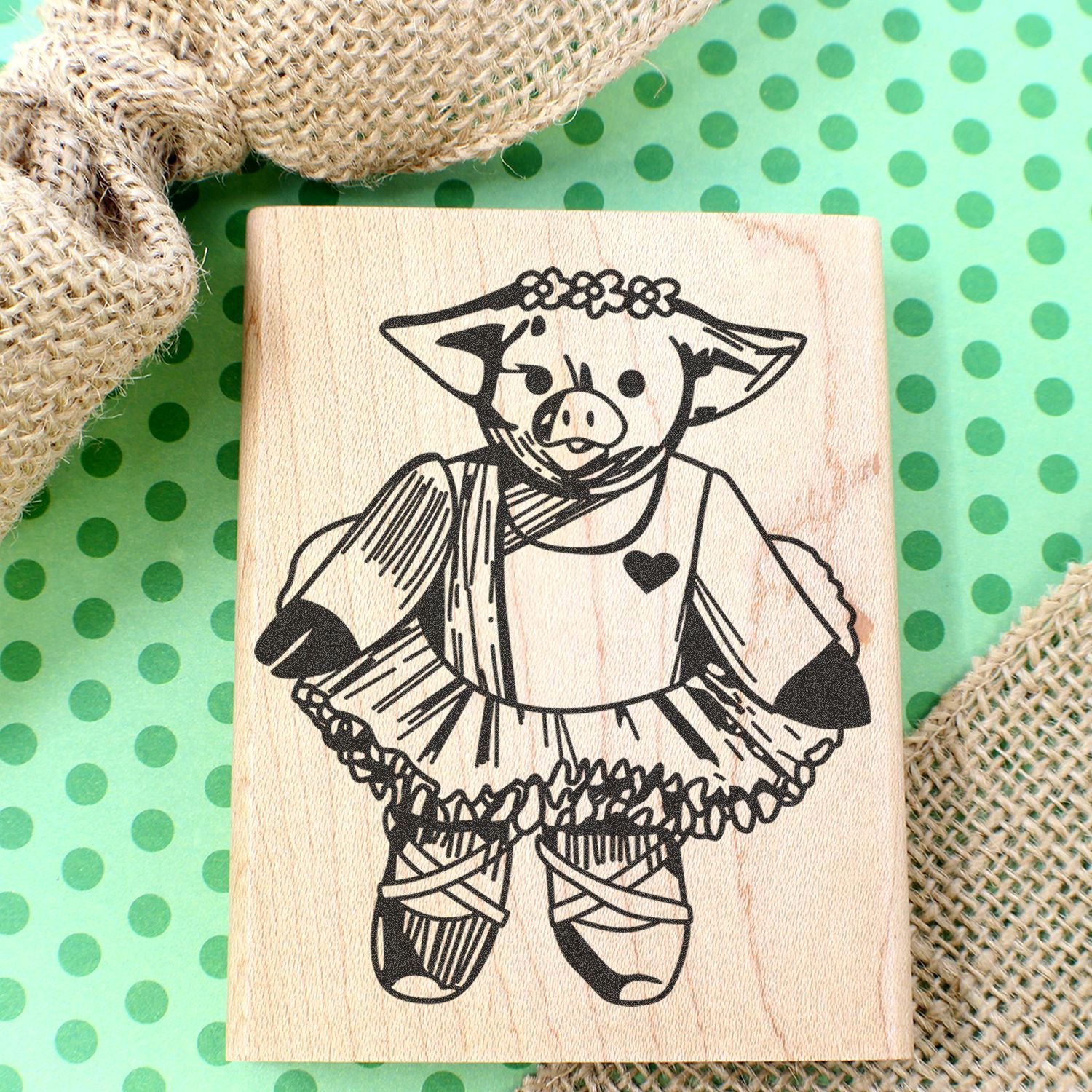 Handmade pig stamp illustration on wooden block with green polka dot background and burlap fabric accents.
