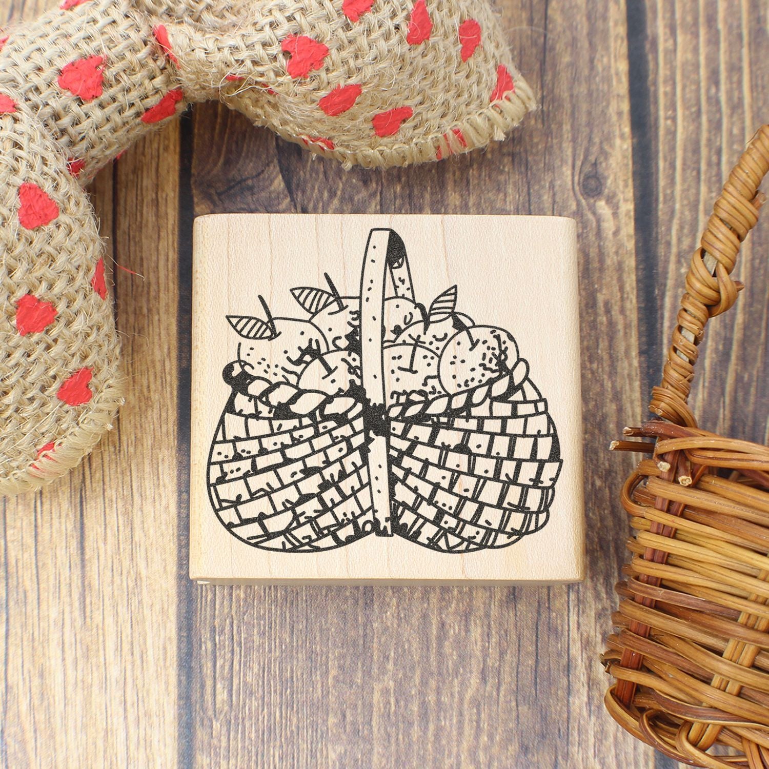 Wooden rubber stamp with basket of apples illustration on a rustic wood background, surrounded by woven craft decor.