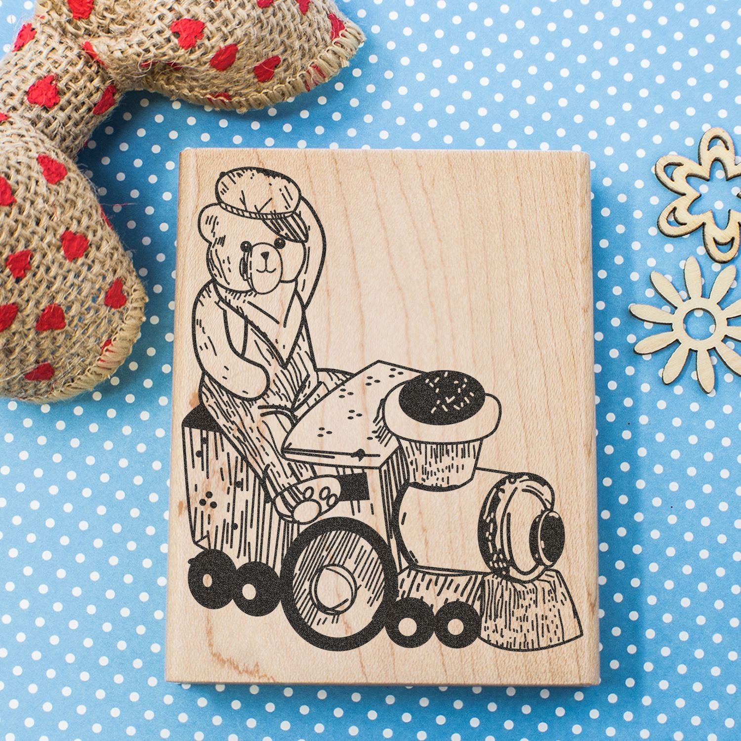 Wooden stamp with teddy bear riding a toy tractor on a blue polka dot background.